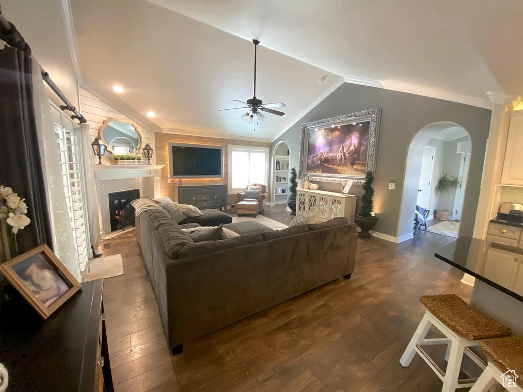 Living room featuring arched walkways, lofted ceiling, crown molding, a fireplace, and ceiling fan