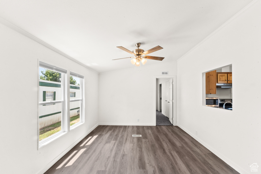 Unfurnished room with dark wood finished floors, ornamental molding, and a ceiling fan