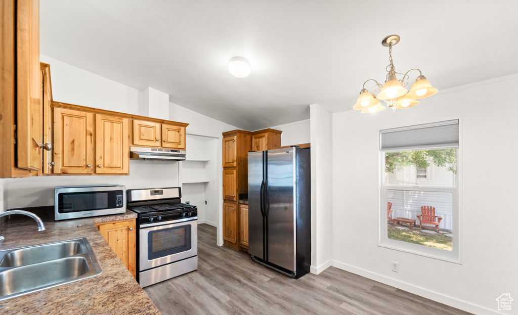 Kitchen featuring stainless steel appliances, under cabinet range hood, vaulted ceiling, a chandelier, and light wood-style flooring