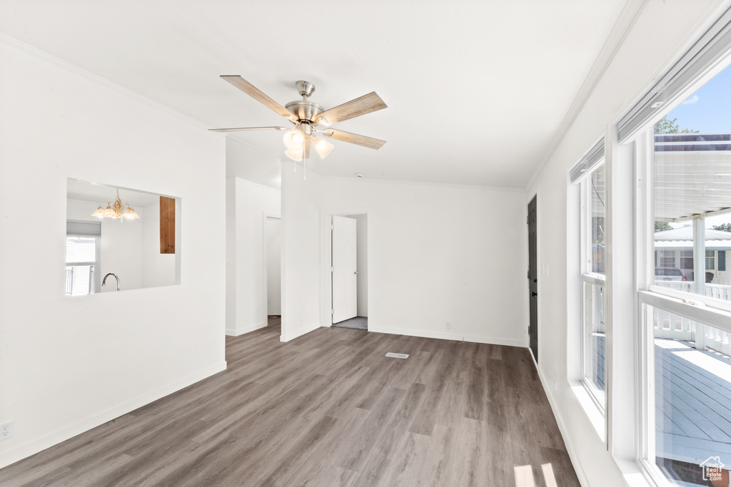 Unfurnished room with wood finished floors, plenty of natural light, a chandelier, ceiling fan, and ornamental molding