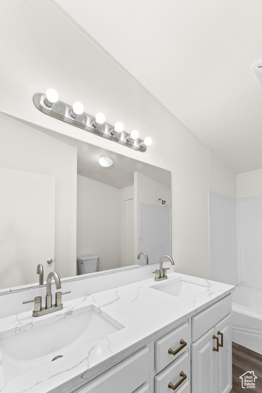 Bathroom with double vanity, wood finished floors, and a bath