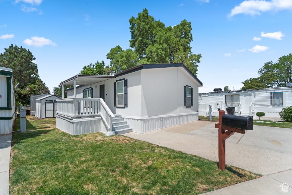 Manufactured / mobile home featuring a storage shed, covered porch, and a front lawn