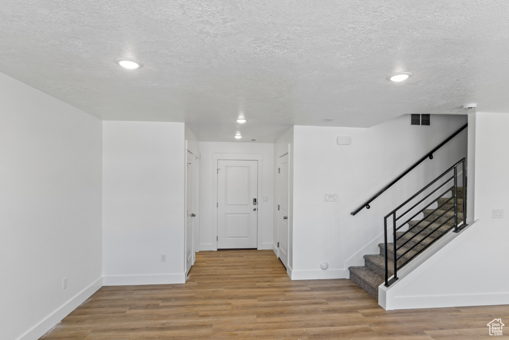Corridor with a textured ceiling, light wood finished floors, stairway, and recessed lighting