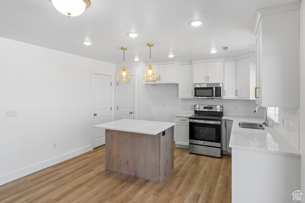 Kitchen featuring stainless steel appliances, light wood-type flooring, tasteful backsplash, light countertops, and white cabinetry