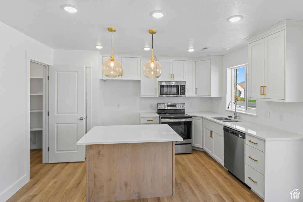 Kitchen with appliances with stainless steel finishes, tasteful backsplash, light wood-style floors, white cabinets, and recessed lighting