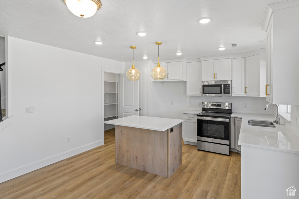 Kitchen featuring stainless steel appliances, light wood finished floors, white cabinets, light countertops, and backsplash