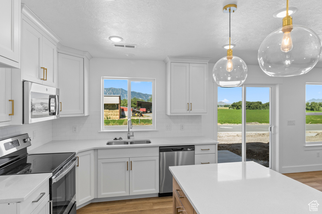 Kitchen with stainless steel appliances, light wood-type flooring, light countertops, white cabinets, and a textured ceiling