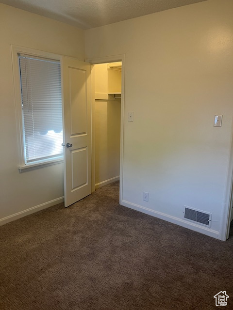 Unfurnished bedroom with dark colored carpet, a spacious closet, and a closet