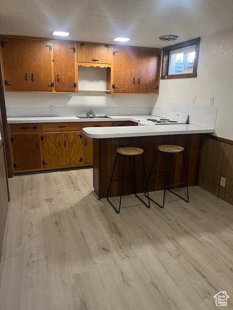 Kitchen featuring a peninsula, brown cabinetry, light wood-style flooring, stove, and light countertops