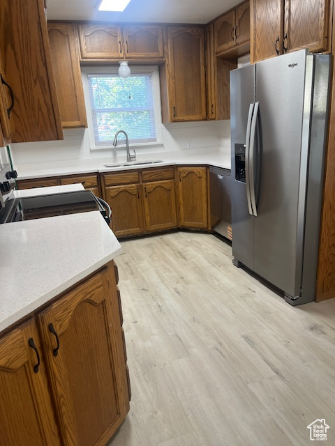 Kitchen with appliances with stainless steel finishes, light wood-style floors, brown cabinetry, and light countertops