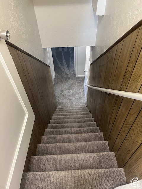 Stairs with a textured wall, carpet flooring, and wooden walls