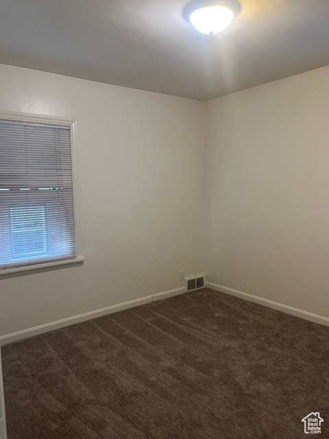 Unfurnished room featuring dark colored carpet and baseboards