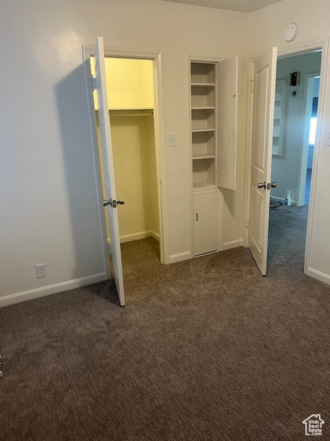 Unfurnished bedroom featuring dark colored carpet and baseboards