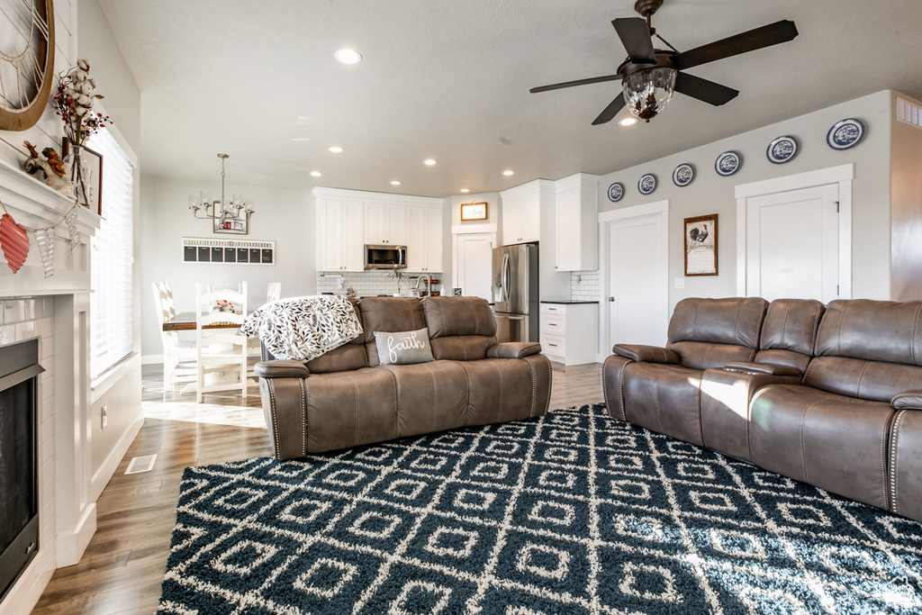 Living room with a tiled fireplace, a ceiling fan, light wood-style floors, recessed lighting, and a chandelier