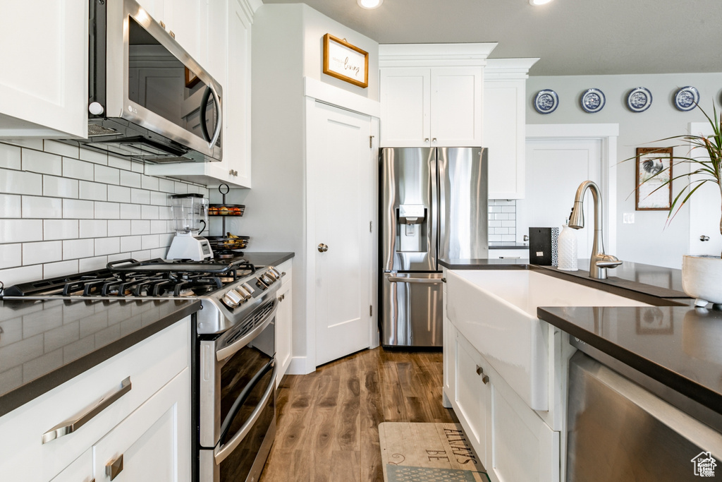 Kitchen with appliances with stainless steel finishes, dark countertops, dark wood-type flooring, white cabinetry, and recessed lighting