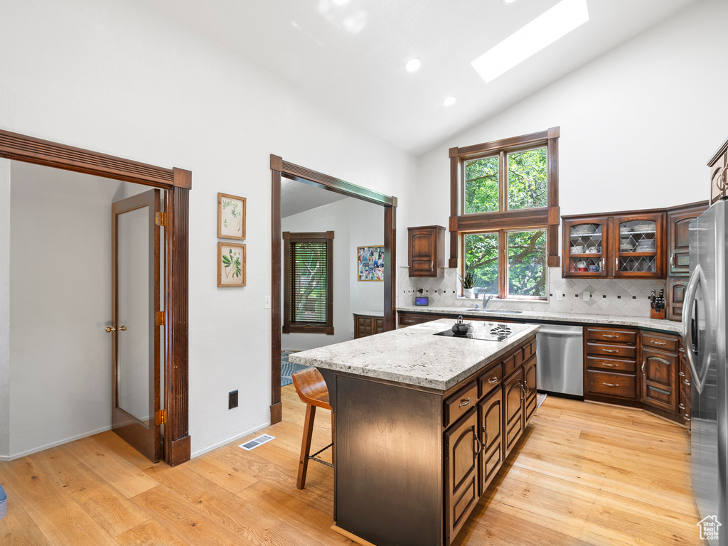 Kitchen featuring appliances with stainless steel finishes, high vaulted ceiling, a skylight, light wood-style floors, and a kitchen island