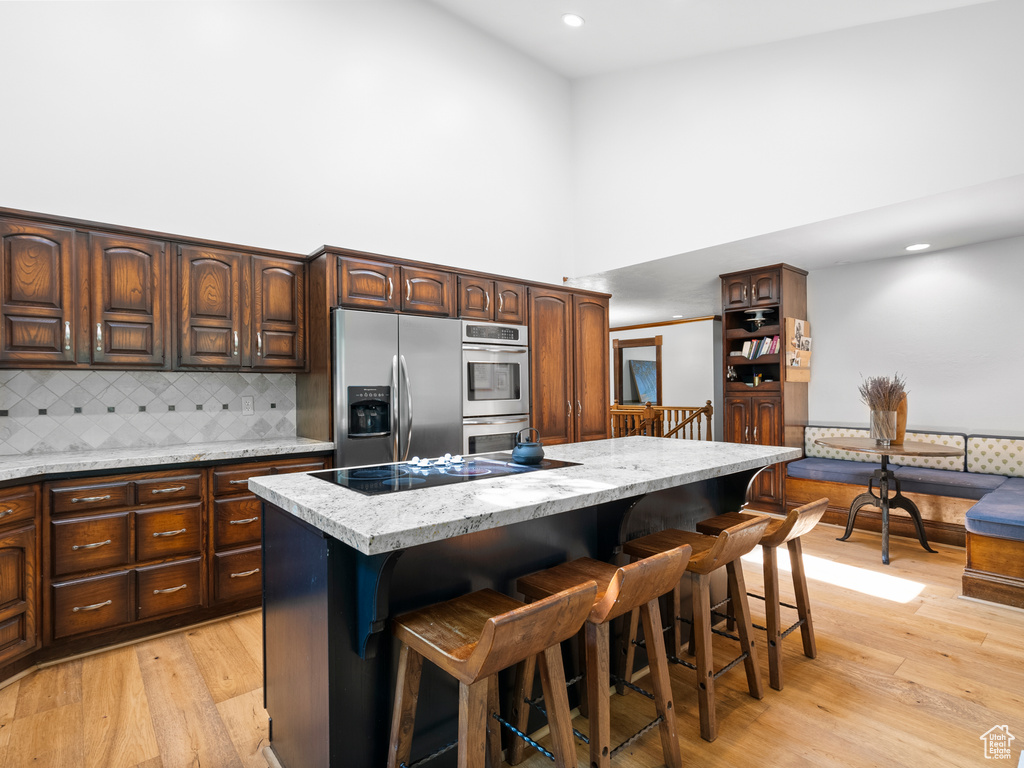 Kitchen with appliances with stainless steel finishes, a towering ceiling, a kitchen island, tasteful backsplash, and light wood-type flooring
