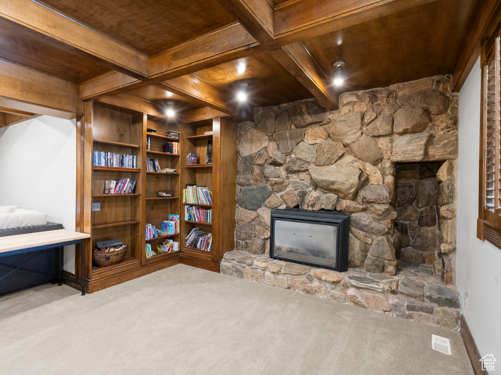 Living room featuring a stone fireplace, carpet flooring, and a wooden ceiling with exposed beams