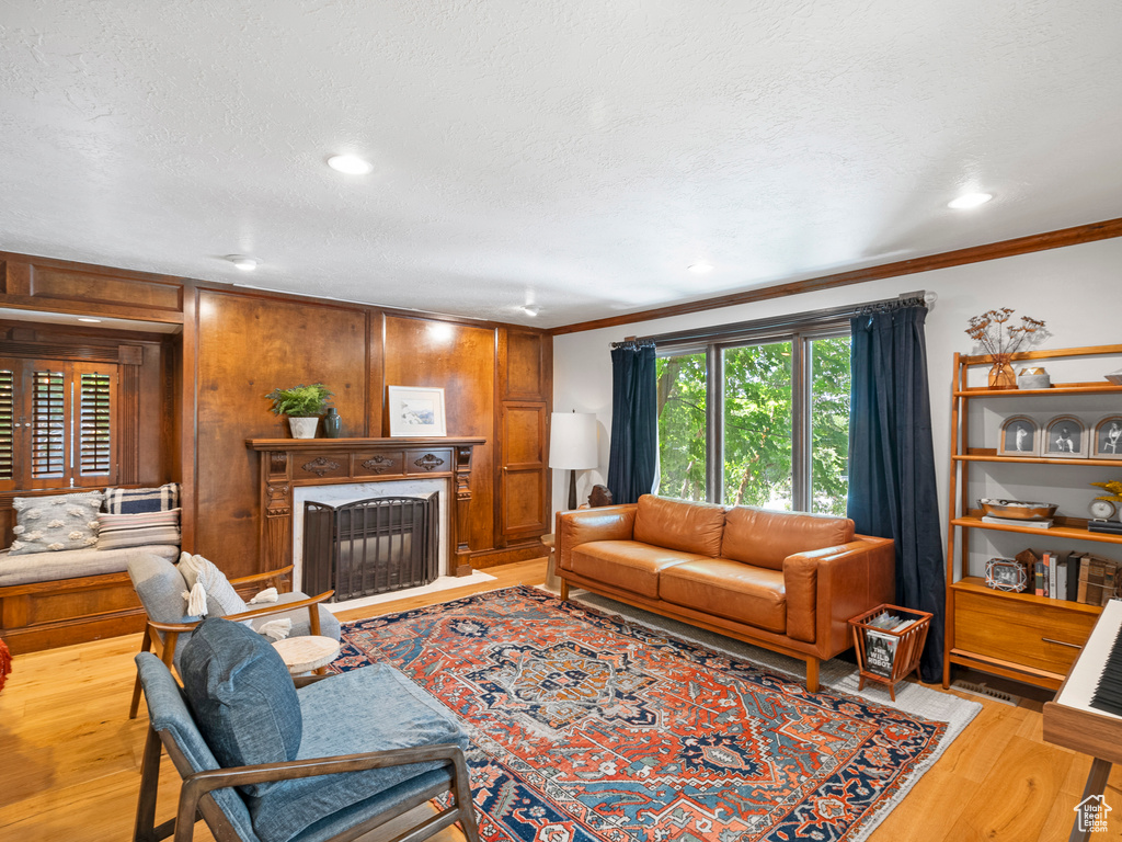 Living room featuring wood finished floors, crown molding, a fireplace with flush hearth, a textured ceiling, and wood walls