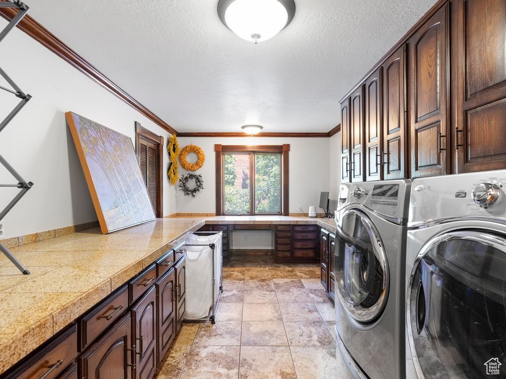 Washroom featuring washing machine and clothes dryer, cabinet space, crown molding, a textured ceiling, and light stone finish flooring