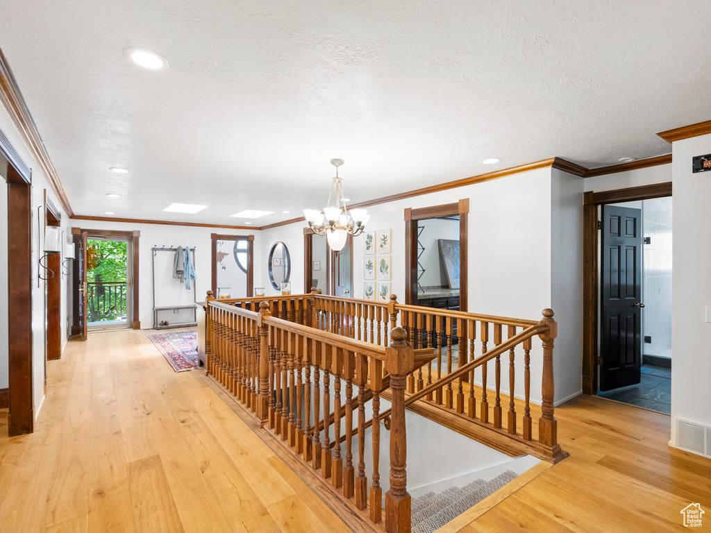 Hallway featuring an upstairs landing, ornamental molding, light wood-type flooring, a chandelier, and recessed lighting