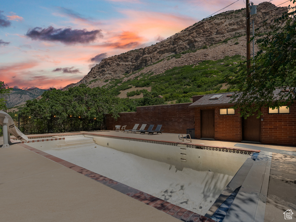 Pool at dusk featuring a mountain view, a patio, and an empty pool