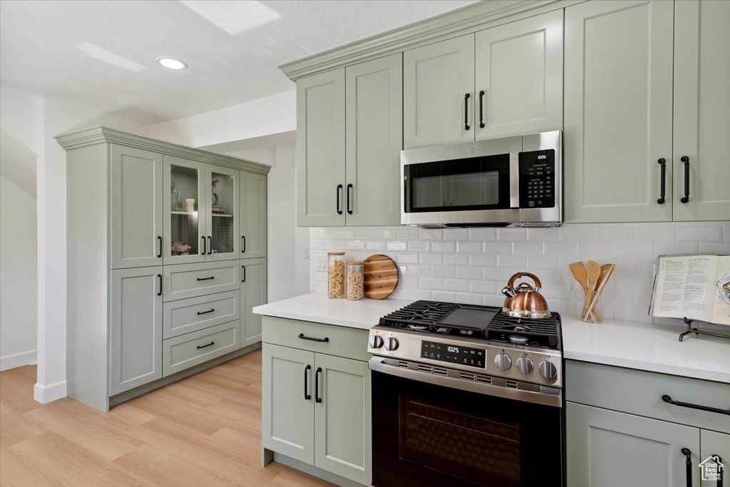 Kitchen with stainless steel appliances, light wood-type flooring, light countertops, decorative backsplash, and recessed lighting