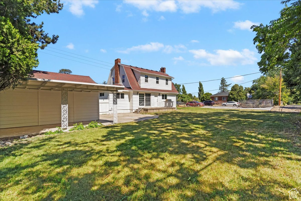 Back of property with a chimney, a patio, a lawn, and a gambrel roof