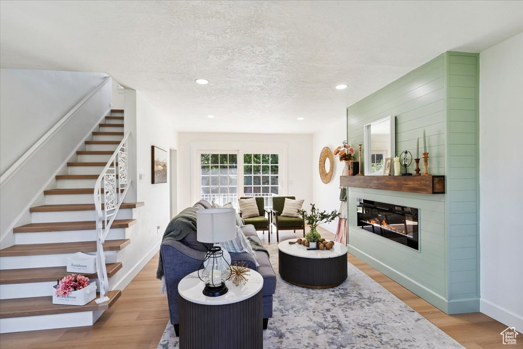 Living room with stairway, light wood-style flooring, a glass covered fireplace, a textured ceiling, and recessed lighting