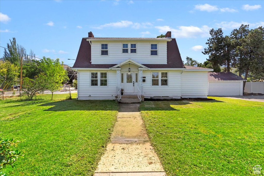 View of front of home with a chimney, a front yard, and a detached garage