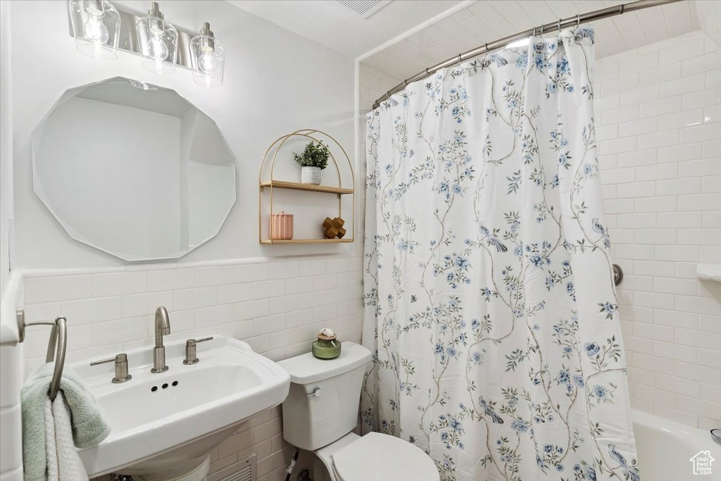 Bathroom with tile walls, shower / bath combo with shower curtain, and a wainscoted wall