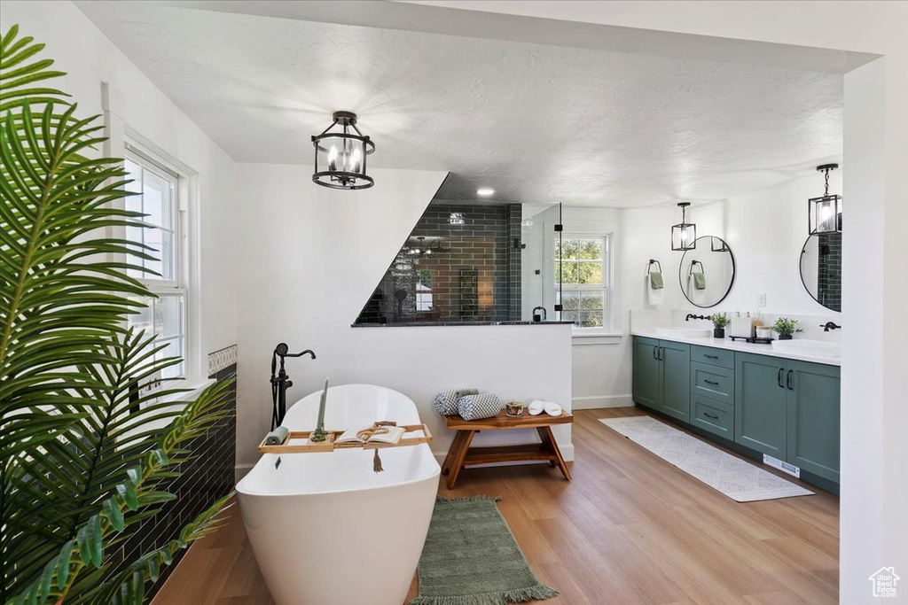 Bathroom with double vanity, wood finished floors, a freestanding bath, walk in shower, and a chandelier
