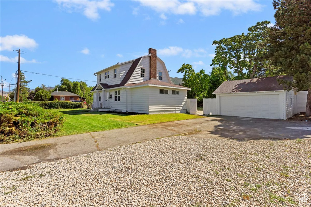 View of side of property with a gambrel roof, a chimney, a garage, a lawn, and an outbuilding