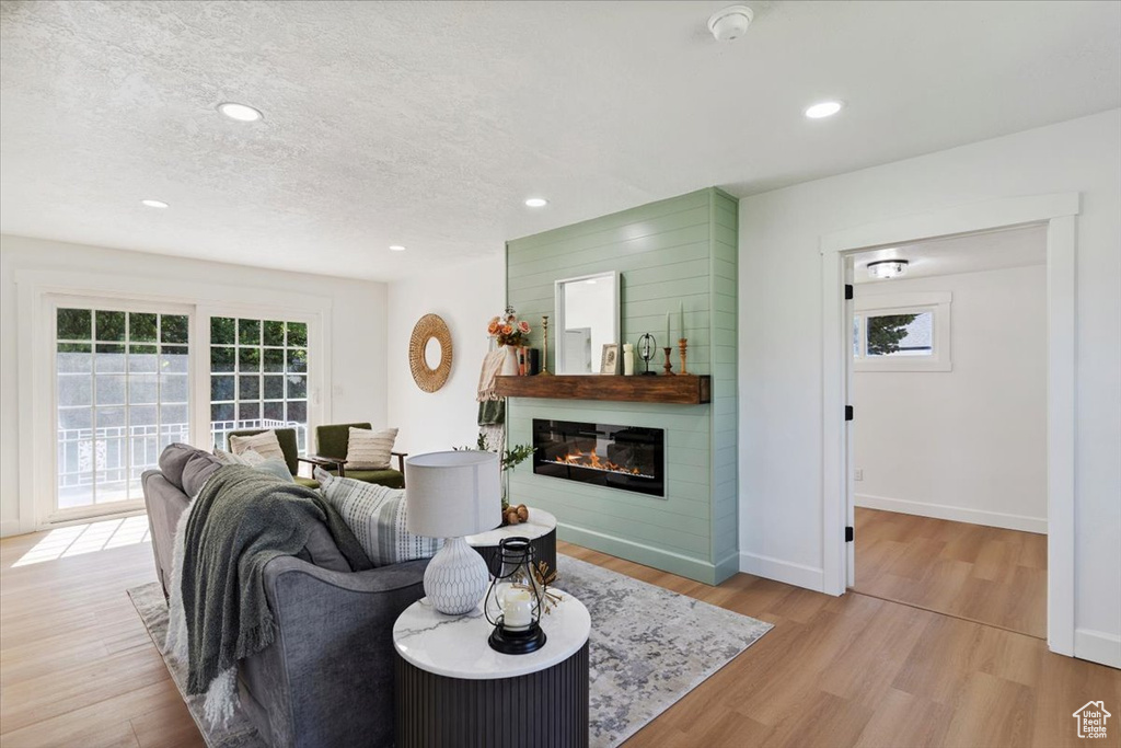 Living room featuring a large fireplace, plenty of natural light, light wood-style floors, a textured ceiling, and recessed lighting