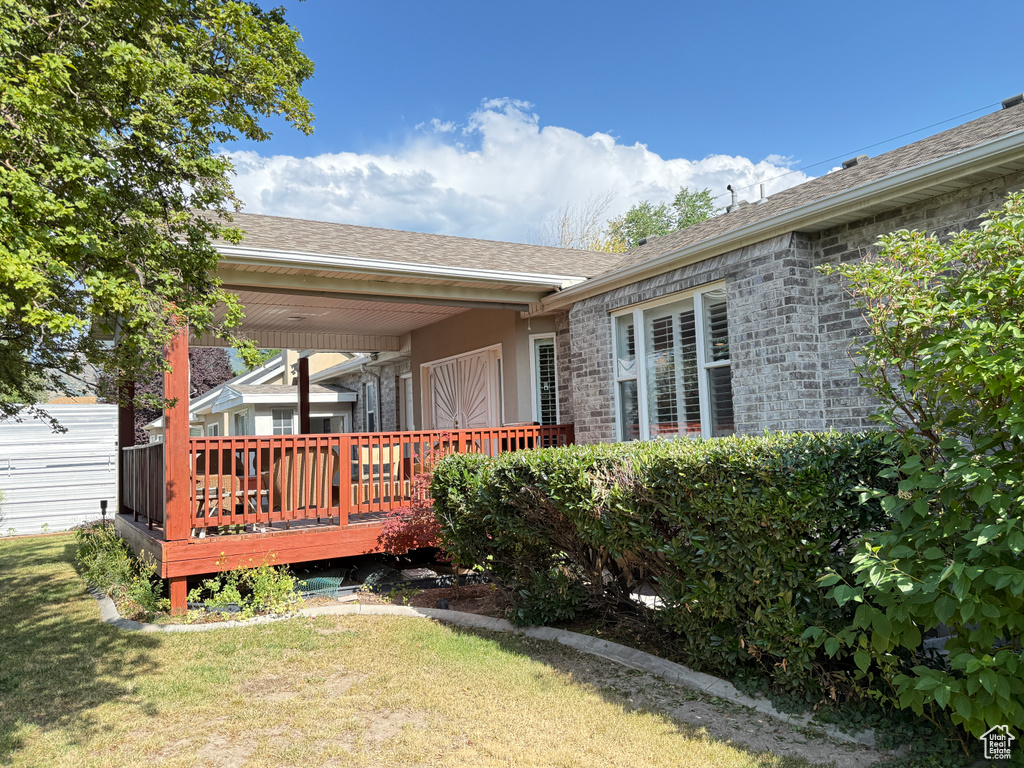 Rear view of property featuring a deck, a yard, a shingled roof, and stone siding