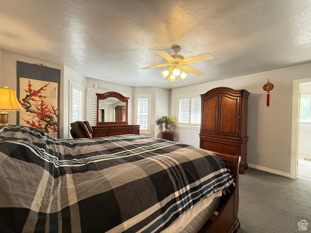 Bedroom with a textured ceiling, multiple windows, dark colored carpet, and a ceiling fan