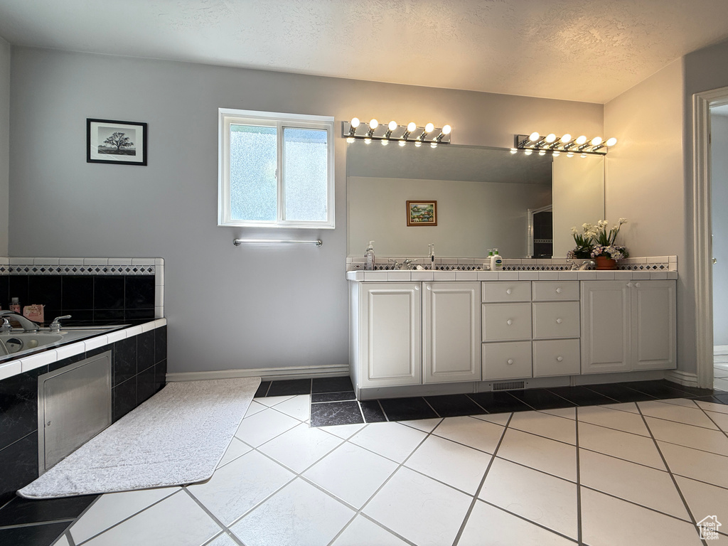 Full bath with double vanity, a textured ceiling, a relaxing tiled tub, and tile patterned flooring