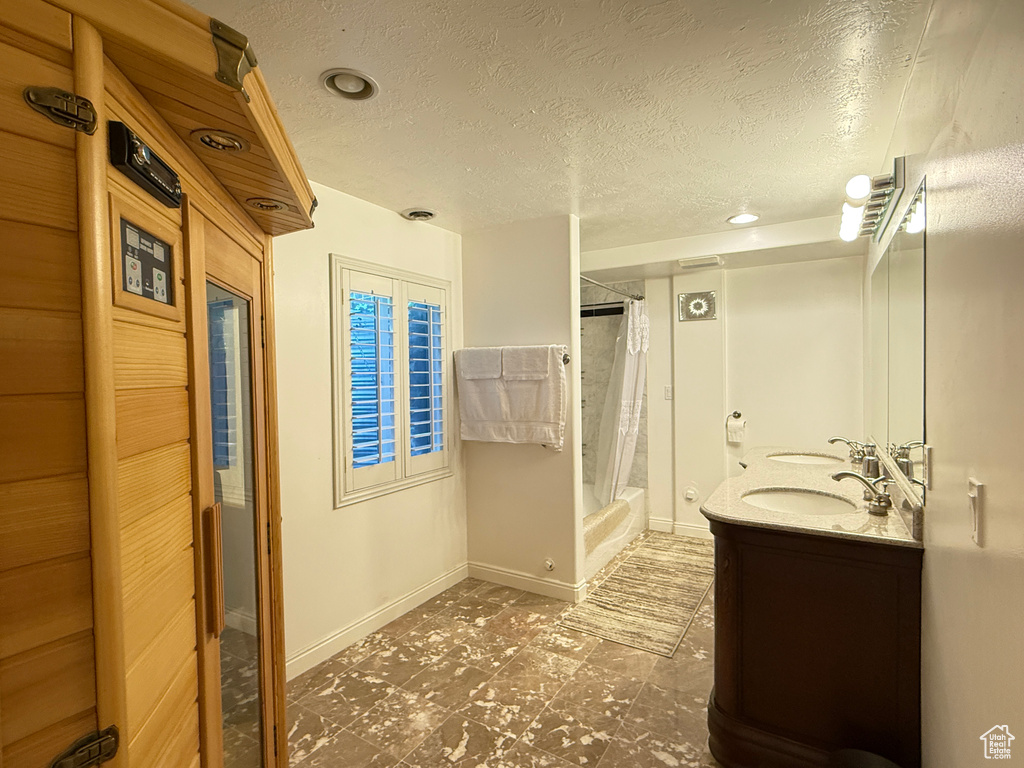 Bathroom with a textured ceiling, double vanity, shower / bathtub combination with curtain, and recessed lighting