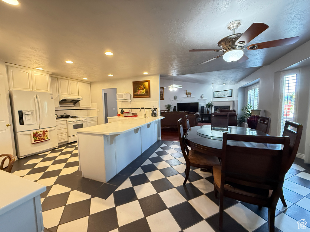 Kitchen featuring white appliances, a ceiling fan, under cabinet range hood, a peninsula, and white cabinets