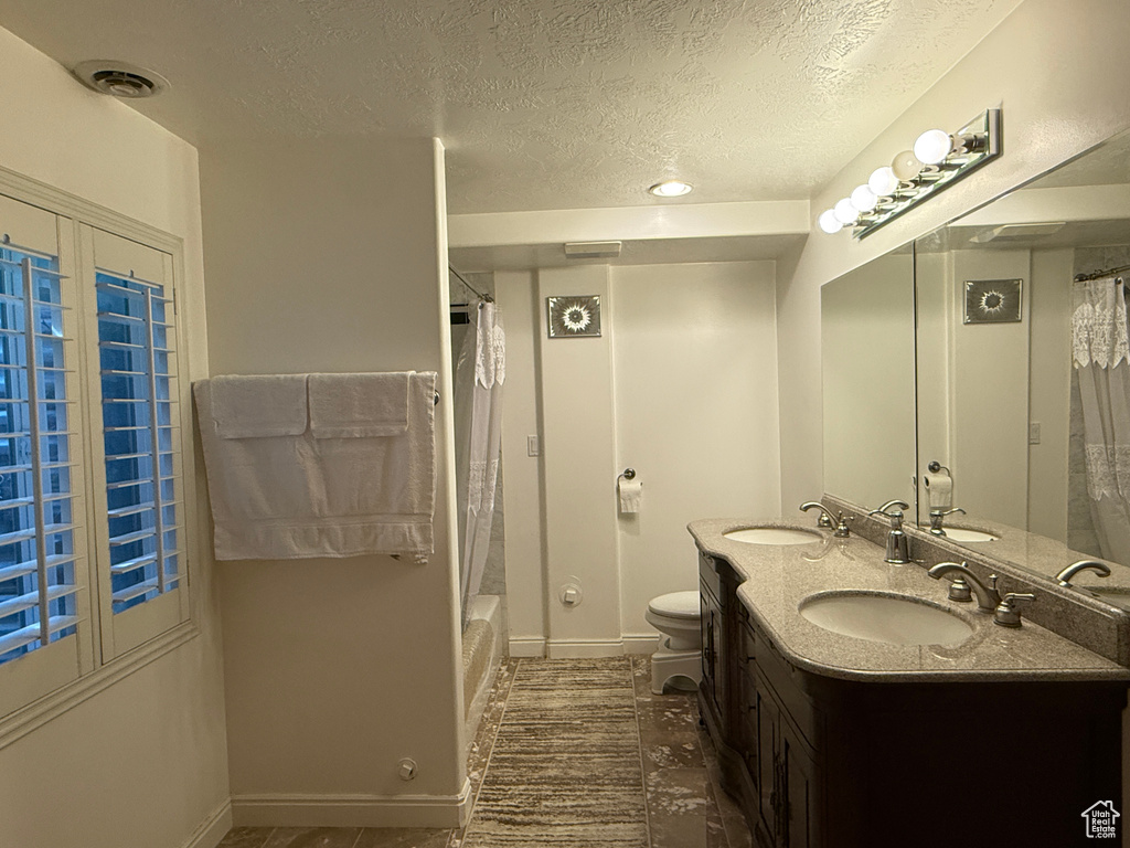 Full bath with a textured ceiling, double vanity, and shower / bath combo with shower curtain