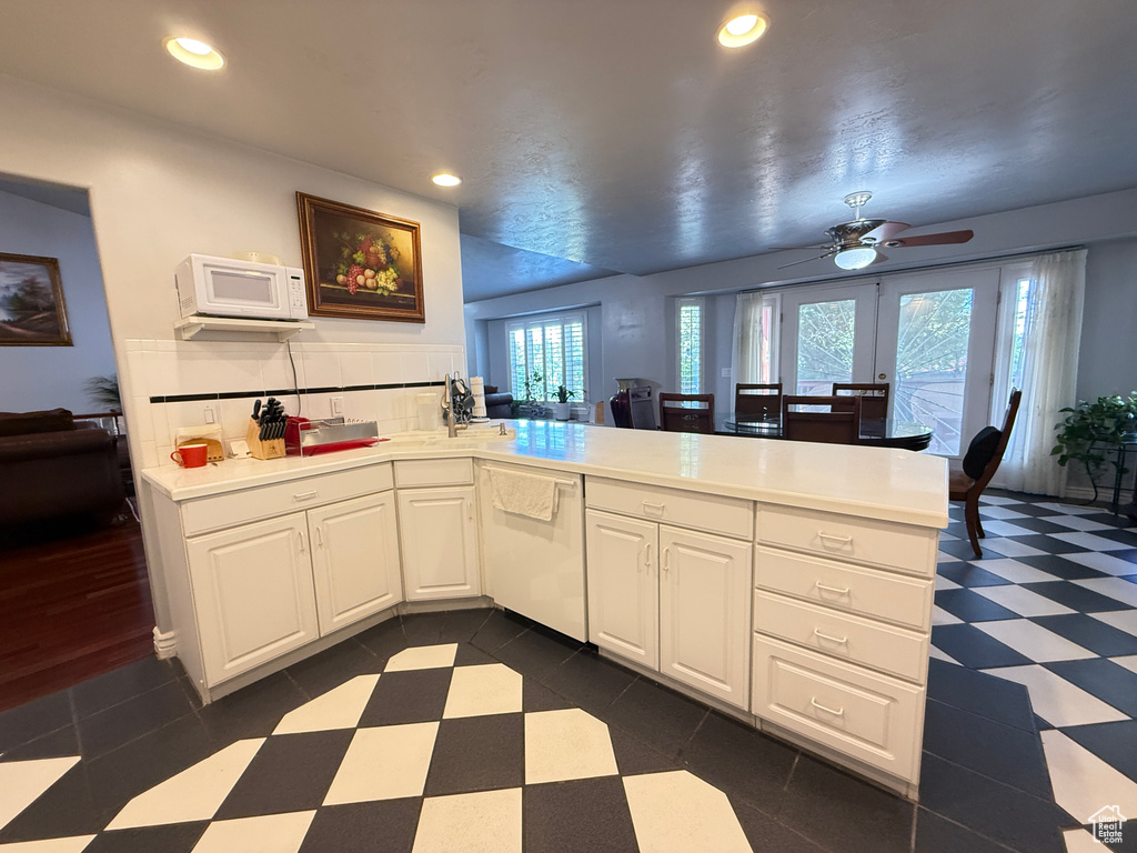 Kitchen featuring white appliances, a peninsula, dark floors, light countertops, and a ceiling fan