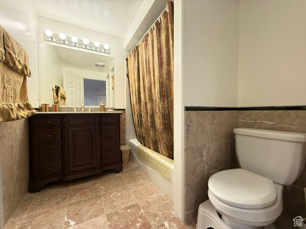Full bathroom with vanity, tile walls, shower / tub combo with curtain, wainscoting, and stone finish flooring