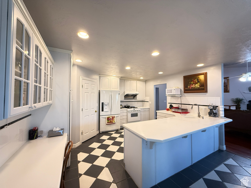 Kitchen with white appliances, dark floors, a peninsula, a breakfast bar, and white cabinetry