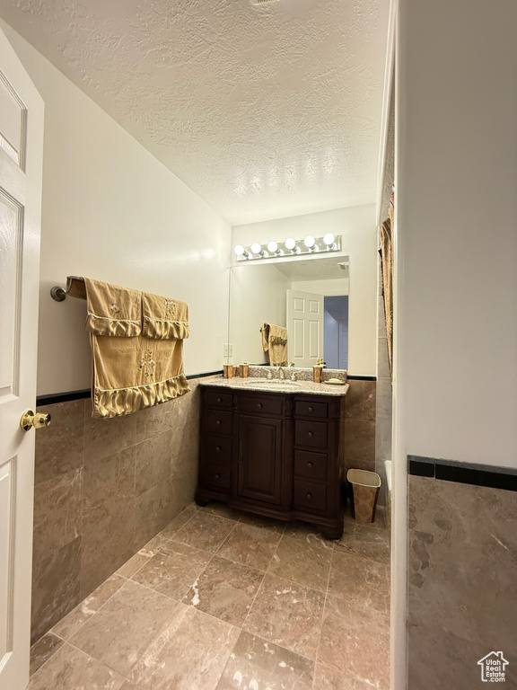 Bathroom featuring tile walls, vanity, a wainscoted wall, a textured ceiling, and stone finish flooring