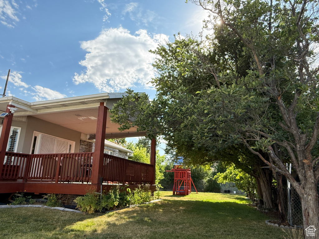 View of green lawn with a playground and a deck