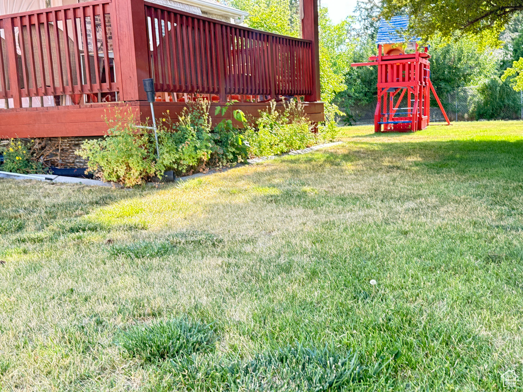 View of green lawn featuring a playground and a wooden deck