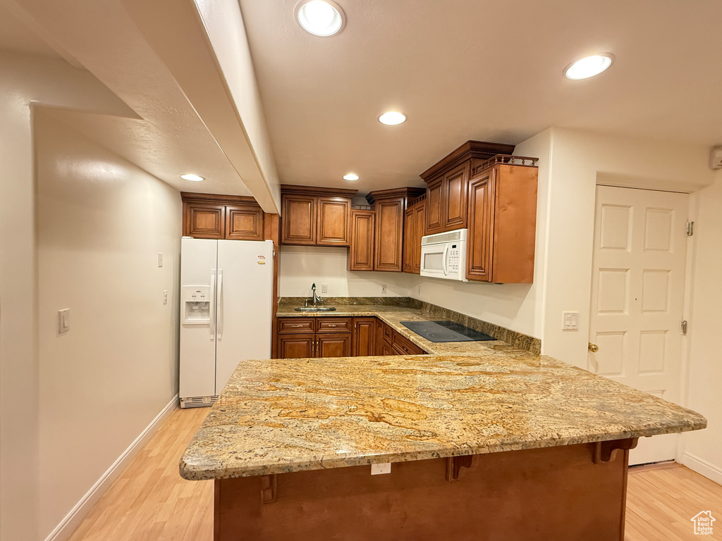 Kitchen featuring white appliances, a peninsula, a breakfast bar area, light wood-type flooring, and recessed lighting