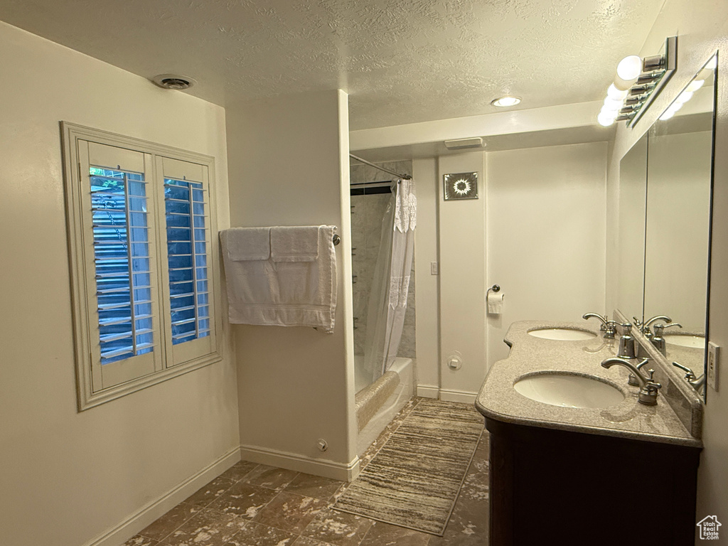 Full bath featuring a textured ceiling, shower / tub combo with curtain, and double vanity
