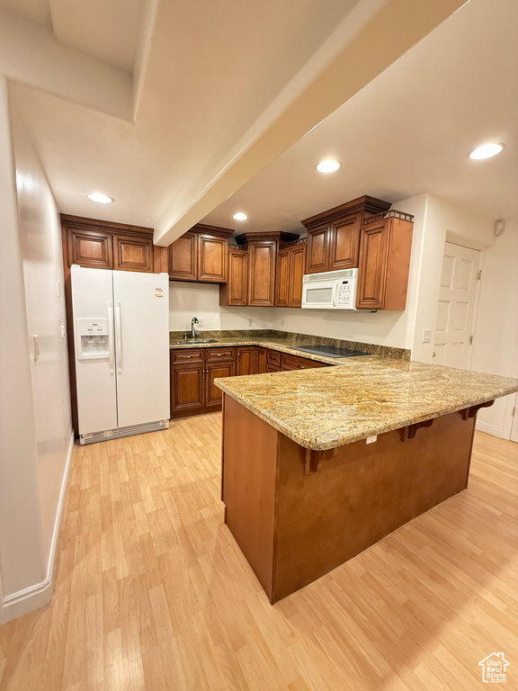Kitchen featuring white appliances, a peninsula, light wood finished floors, a breakfast bar area, and light stone counters