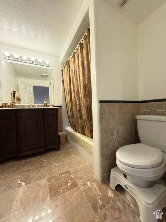 Bathroom with vanity, tile walls, shower / tub combo, wainscoting, and stone finish flooring